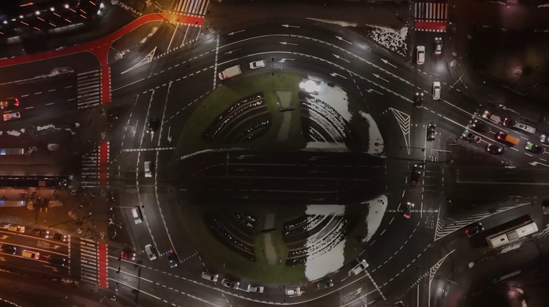 Luftaufnahme eines beleuchteten Kreisverkehrs mit mehreren Fahrzeugen und angrenzenden Straßen in der Nacht